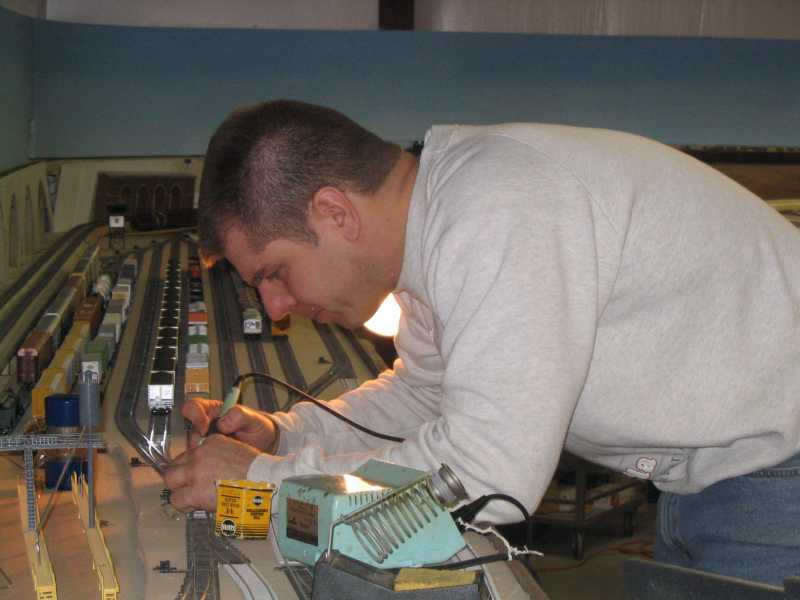 Scott Kurzawski uses his soldering iron to repair a turnout leading to Conroe Yard on the layout of APN